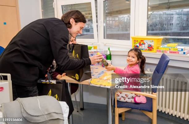 Nico Schulz of Borussia Dortmund hands over gifts to a kid during the annual visit at the Children's Hospital on December 04, 2019 in Dortmund,...