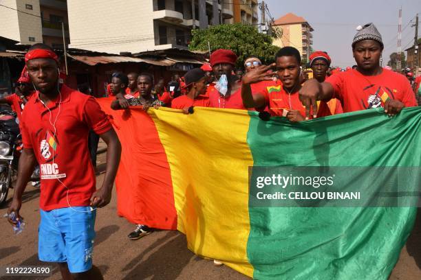 Demonstrators walk behind a giant Guinea's national flag on January 6, 2020 in Conakry, as they take part in an anti-government rally to protest...