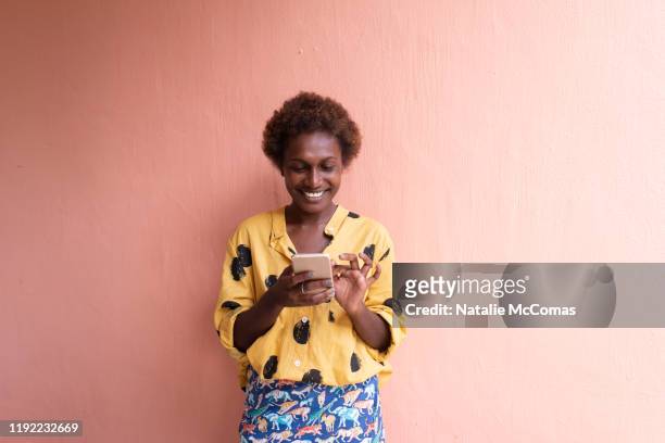 one young woman in front of pink wall smiling on mobile phone - the project portraits stock pictures, royalty-free photos & images