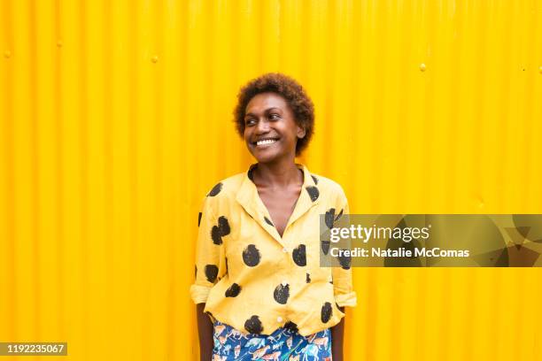 one young woman smiling in front of yellow wall - melanesia stock pictures, royalty-free photos & images