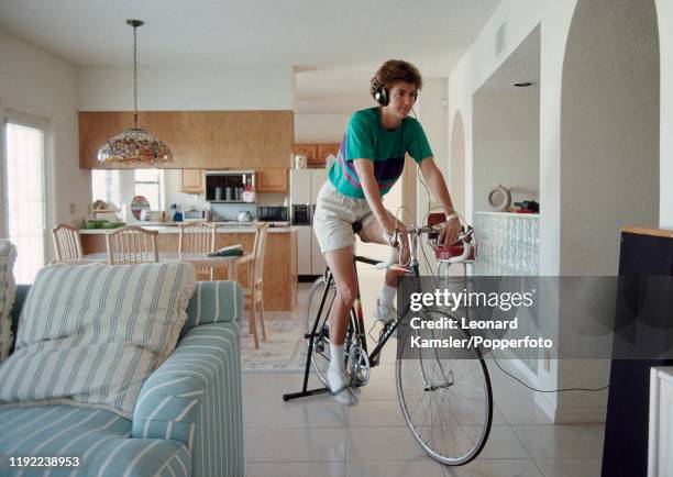 American golfer Beth Daniel wearing headphones whislt pedalling her stationary exercise bicycle at home, circa 1990.