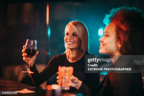 zwei frauen halten ihre getränke, während sie an der bartheke in einem club sitzen - cocktail counter stock-fotos und bilder