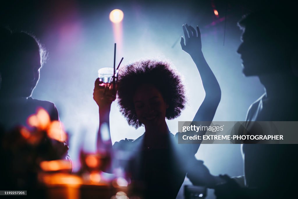 Silhouette d'une fille avec une danse afro avec un cocktail dans sa main dans une boîte de nuit
