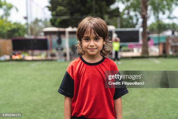 verticale de garçon mignon restant sur le terrain de football - tenue de football photos et images de collection