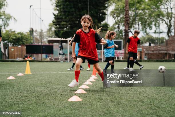 vastbesloten meisje beoefenen voetbal oefeningen op veld - boy girl stockfoto's en -beelden