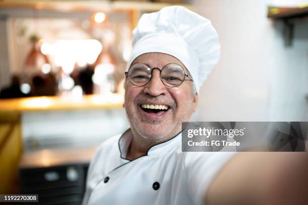 senior chef taking a selfie in a kitchen - chef male kitchen stock pictures, royalty-free photos & images