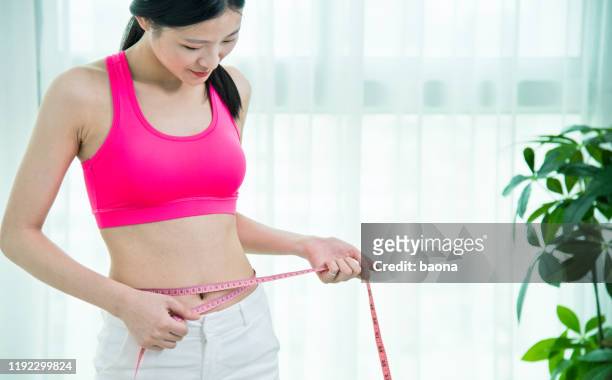 young asian woman measuring her waist - flat stomach stock pictures, royalty-free photos & images