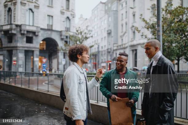 drei junge männer mit einkaufstaschen im regen spazieren - chubby man shopping stock-fotos und bilder