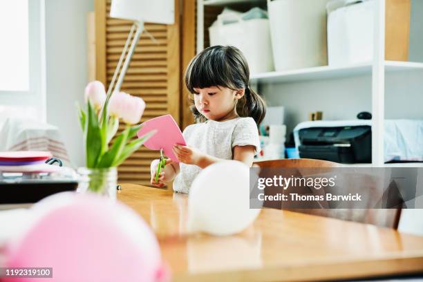 young girl cutting out heart while making valentines day card in home - child cutting card stock pictures, royalty-free photos & images