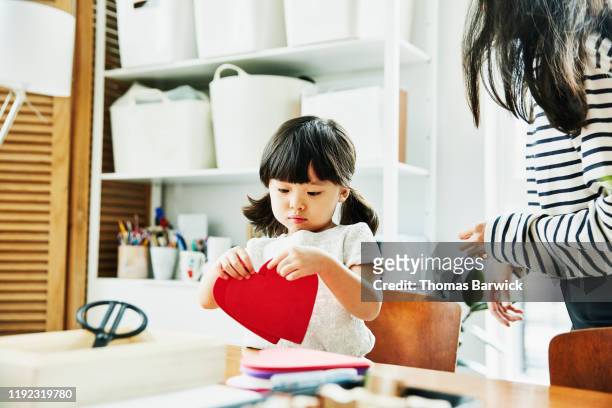 young girl looking at paper hearts while making valentines day cards in home - heart vs mind stockfoto's en -beelden