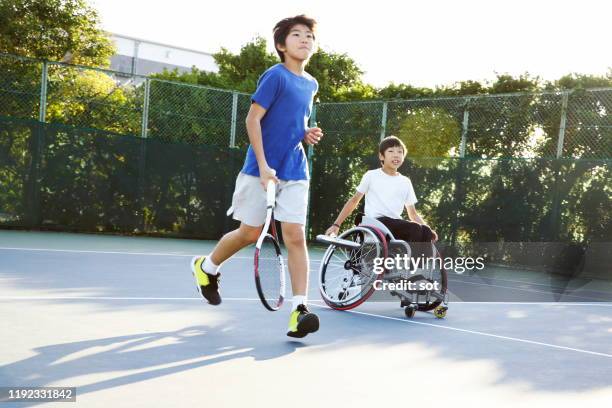 a teenage boy running with another teenage boy in a wheelchair on a tennis court - japanese tennis photos et images de collection