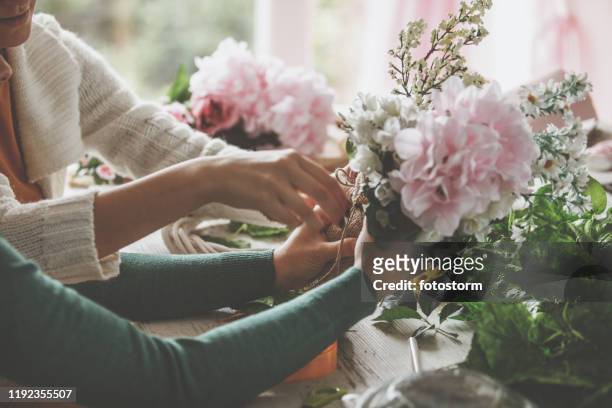 midsection of two unrecognizable young women tying a piece of twine on a bouquet of flowers - hands tied up stock pictures, royalty-free photos & images