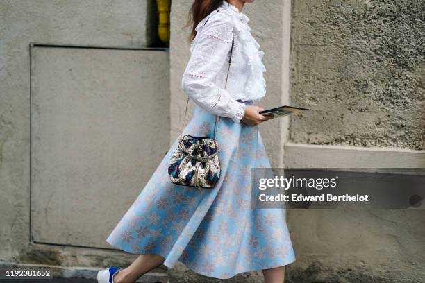 Guest wears a white broderie anglaise long sleeves blouse with a bib and a frill collar, a colorful crocodile bag, a light blue skirt with lace...