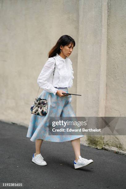 Guest wears earrings, a white broderie anglaise long sleeves blouse with a bib and a frill collar, a colorful crocodile bag, a light blue skirt with...