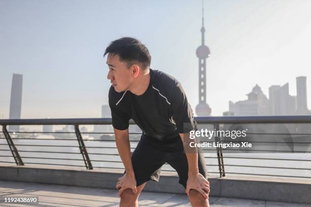 runner taking a break along huangpu river at dawn, with skyline of lujiazui financial district on the bund, shanghai - asian man exercise stock pictures, royalty-free photos & images