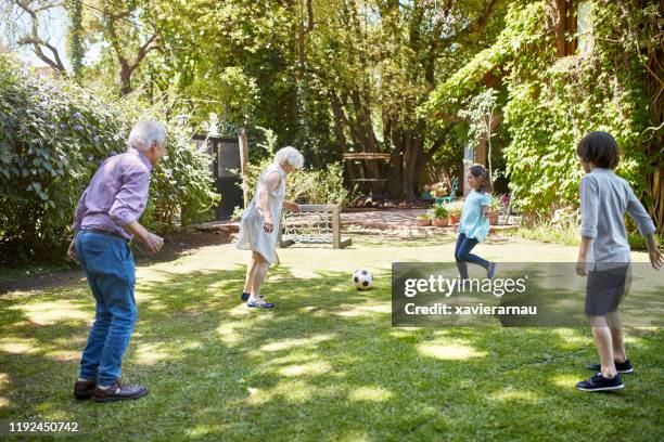 active senior footballers kicking ball with grandchildren - senior kicking stock pictures, royalty-free photos & images