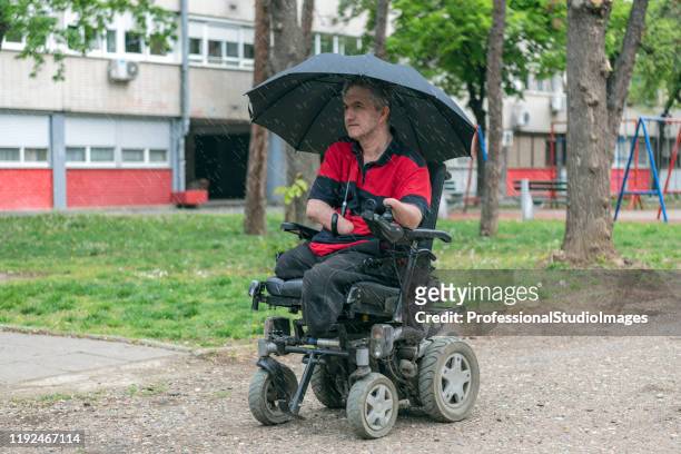 disabled man in electric wheelchair on the move on a rainy day - motorized wheelchair stock pictures, royalty-free photos & images