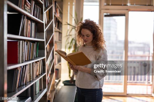 junge frau liest ein buch in der wohnung - books collection stock-fotos und bilder