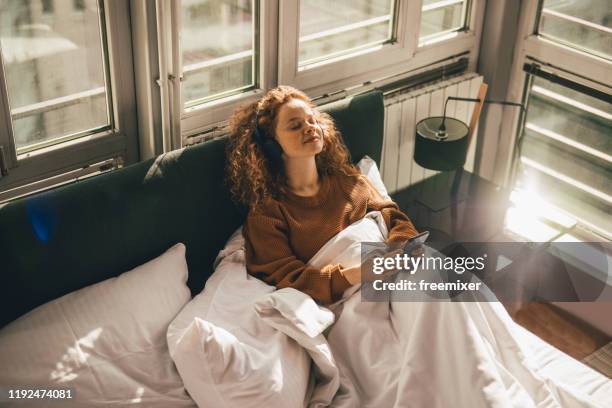 jonge vrouw zittend op bed en het gebruik van mobiele telefoon - awake day stockfoto's en -beelden