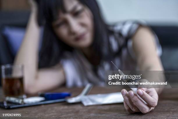 syringe and drugs with out of focus female drug addict sitting - self harm stock-fotos und bilder