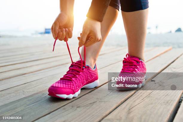 woman tying shoes on the beach - pink shoe stock pictures, royalty-free photos & images