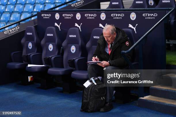 Commentator Martin Tyler takes notes as he sits on the team bench prior to the Premier League match between Manchester City and Manchester United at...