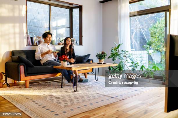 young couple spending time watching tv at home - comfortable couple stock pictures, royalty-free photos & images