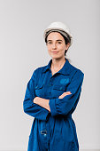 Pretty young cross-armed female engineer in blue workwear and safety helmet
