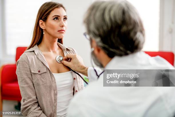 junge frau bekommt ihre schmerzhafte brust von einem arzt untersucht. - adult patient with doctor and stethoscope stock-fotos und bilder