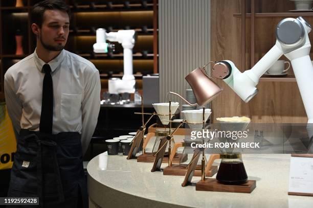 Man dressed in a barrista's outfit watches as an LG CLOi CoBot Barista robot makes pour-over coffee, at the LG booth, January 8, 2020 at the 2020...