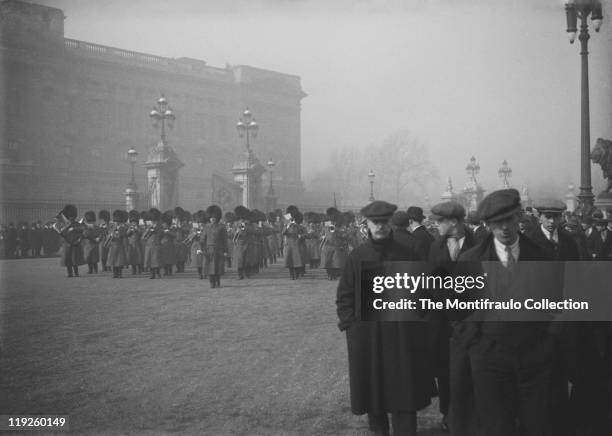 Large crowds standing close to the open gates of Buckingham Palace, London as a military brass band in bearskin hats passes by the Queen Victoria...