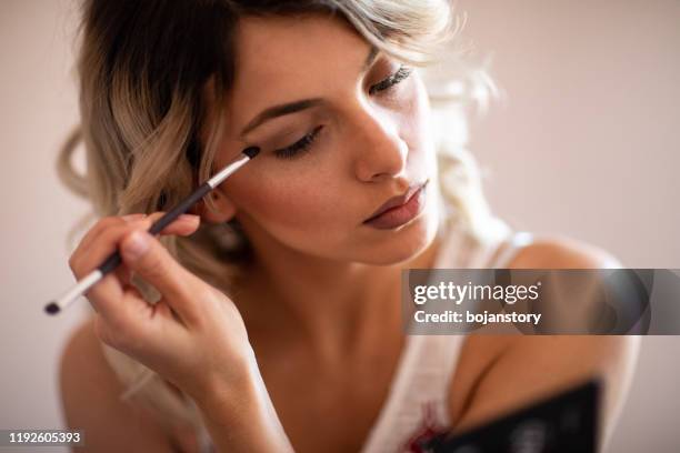 beautiful young woman applying eyeshadow - eyeshadow stock pictures, royalty-free photos & images