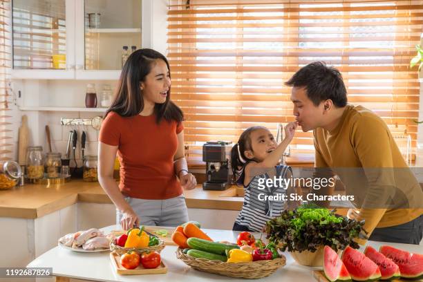 happy young asian family preparing and cooking healthy food in kitchen, family relaxing and spending time together at home - asian family cooking stock pictures, royalty-free photos & images