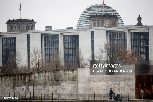 Woman pushes a pram along a concrete wall on Ludwig Erhard Ufer along river Spree on January 9, 2019 near the German parliament in Berlin. - Rain and...