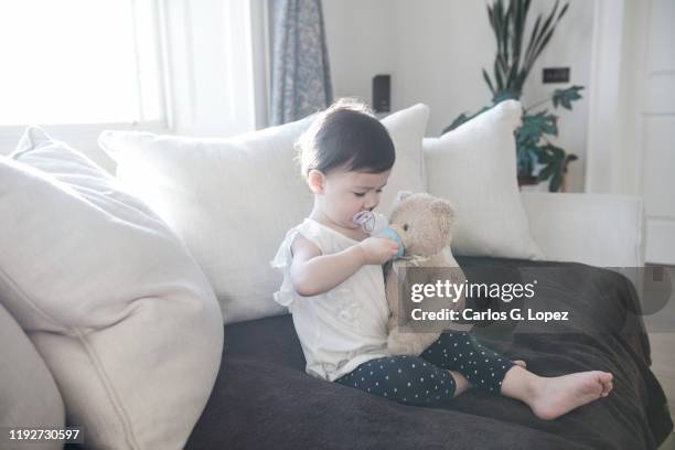 child pretends to feed water to her teddy bear toy while sitting on a sofa - rpg stock-fotos und bilder