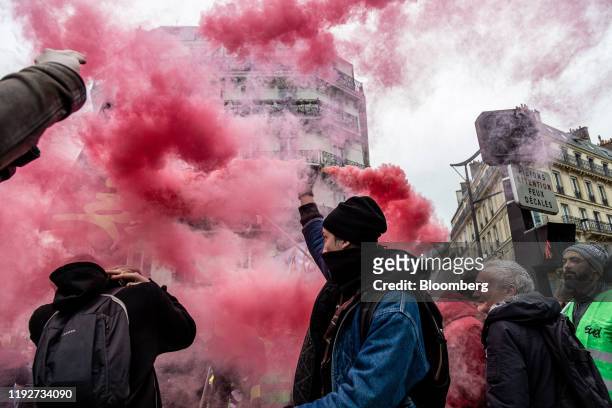 Protester waves an ignited red smoke flare during a day of protest and ongoing transport worker strikes over French pension reform plans in Paris,...
