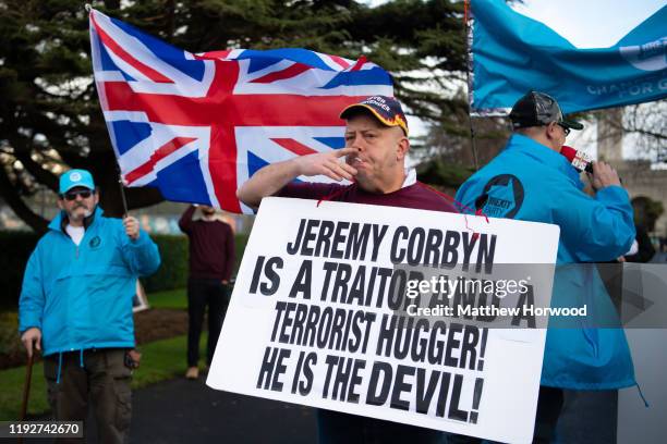 Man holds a sign with a message calling the leader of the Labour Party Jeremy Corbyn a 'traitor' alongside protestors dressed in Brexit Party...