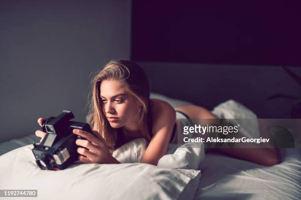 女性の美しさは、ベッドでヴィンテージフォトカメラをチェックアウト - 魅惑的な女性 ストックフォトと画像