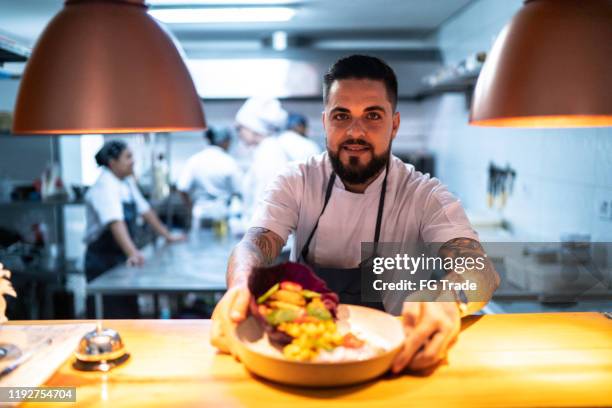 porträt des kochs, der sein fertiggericht zeigt - chefs cooking stock-fotos und bilder