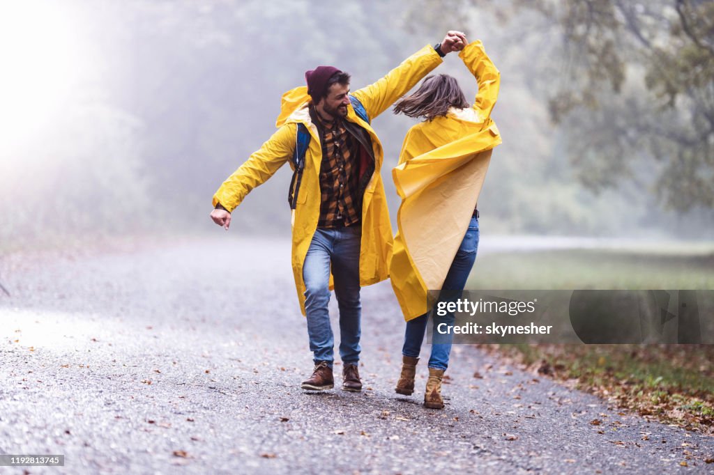 Gelukkig paar in regenjas met plezier tijdens het dansen op een regen in mistige bos.