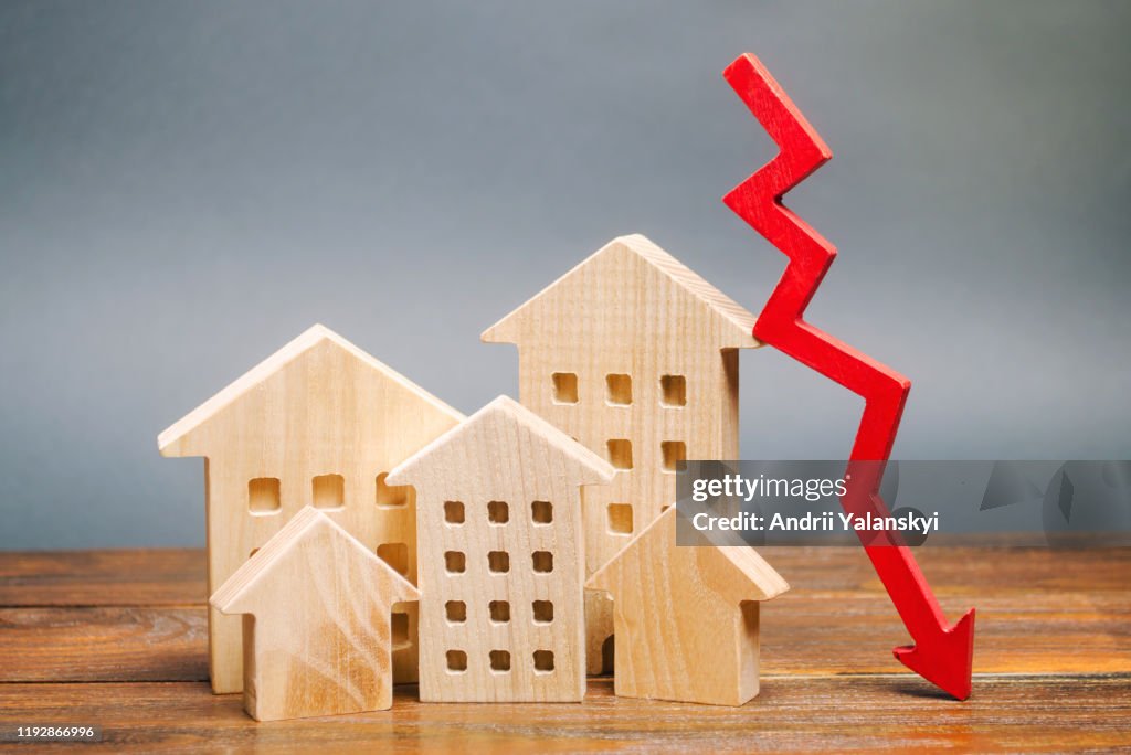 Miniature wooden houses and a red arrow down. The concept of low cost real estate. Lower mortgage interest rates. Falling prices for rental housing and apartments. Reducing demand for home buying