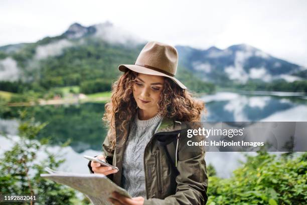 a young woman tourist with backpack on a hiking trip, using smartphone and map. - woman map stock pictures, royalty-free photos & images