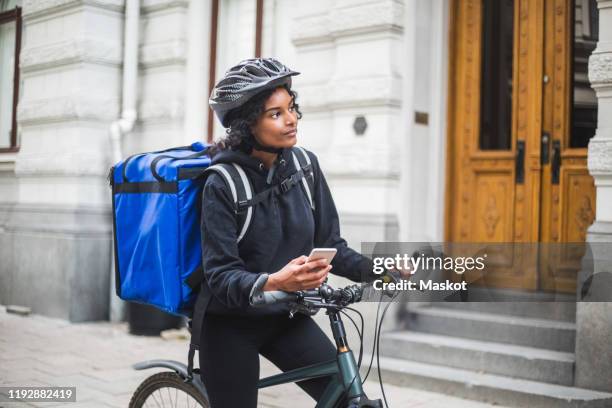 food delivery woman looking away while holding smart phone in city - gig economy stock pictures, royalty-free photos & images