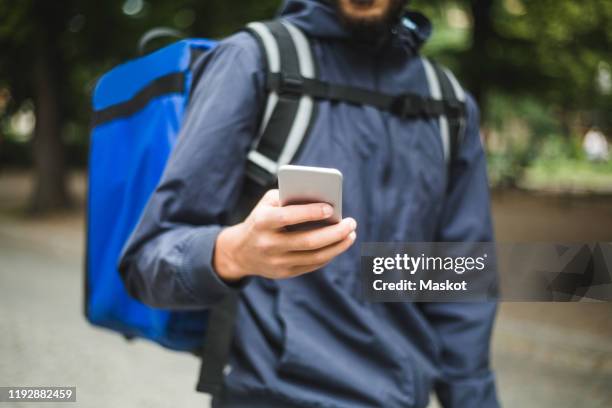 midsection of food delivery man using smart phone in city - gig economy stock pictures, royalty-free photos & images