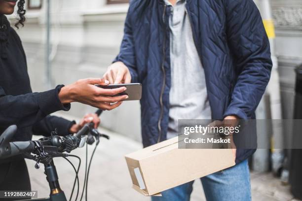 midsection of delivery woman taking sign from male customer while delivering package on sidewalk in city - bike messenger stock pictures, royalty-free photos & images