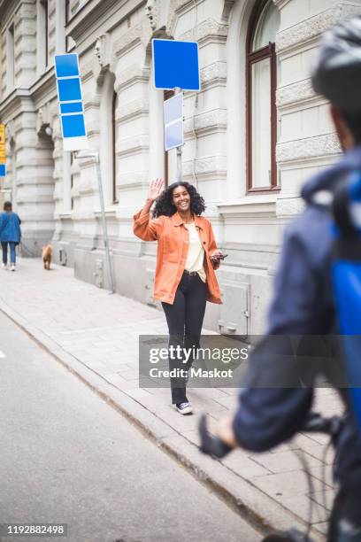 smiling female customer waving hand to delivery man while walking on sidewalk - female waving on street stock pictures, royalty-free photos & images