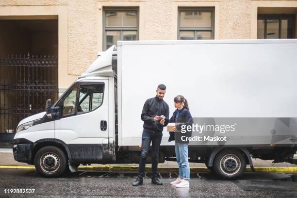 young woman signing on mobile phone while receiving package from male mover - camion blanc photos et images de collection
