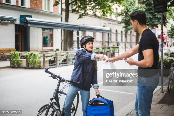 food delivery woman giving package to male customer standing on sidewalk in city - bicycle courier stock pictures, royalty-free photos & images