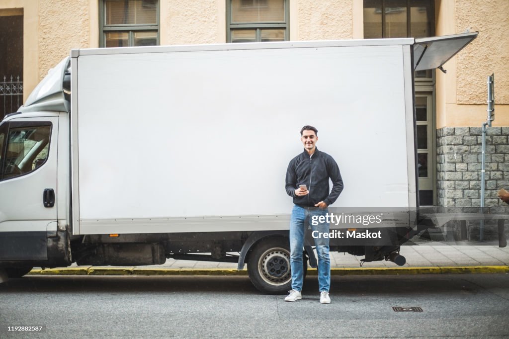 Portrait of male mover standing against truck on street in city