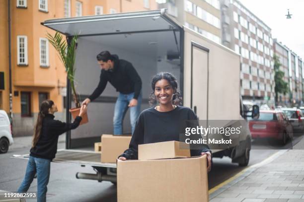 portrait of confident female mover carrying cardboard boxes - removal men imagens e fotografias de stock